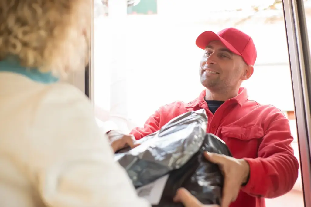 Courier in a red uniform handing a parcel to a customer at the front door of their home