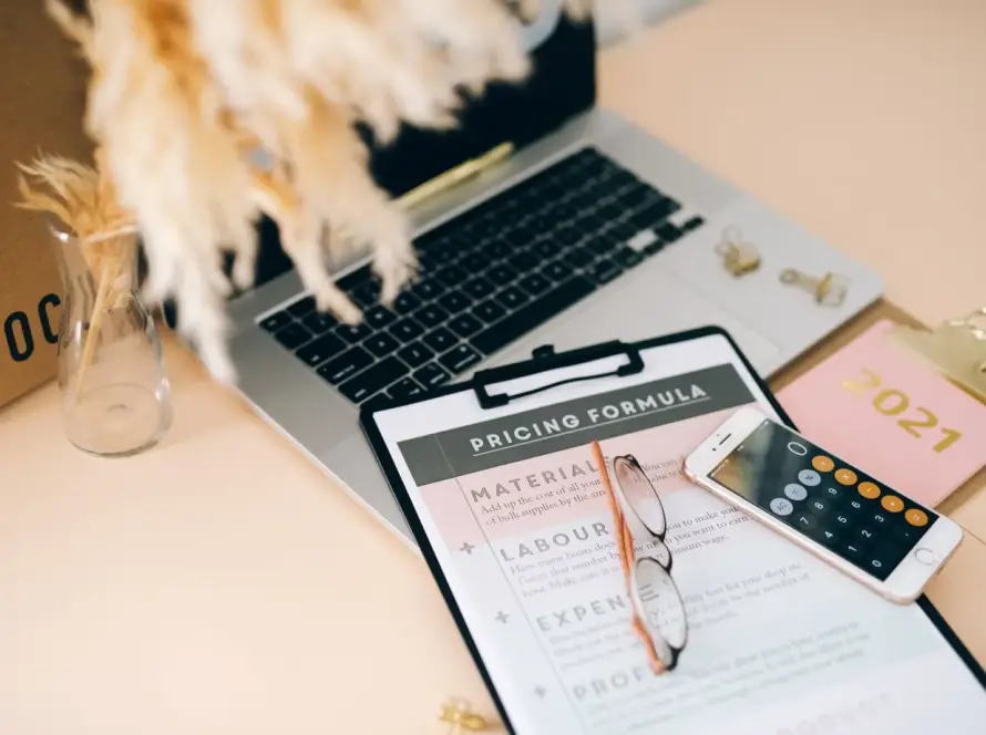 Sullo schermo di un laptop viene visualizzato un modello di formula di prezzo con sezioni per Materiali, Manodopera, Spese e Profitto, con occhiali da lettura e una calcolatrice per smartphone accanto, a rappresentare la struttura di base per la valutazione delle componenti di prezzo dei servizi di logistica conto terzi (3PL).